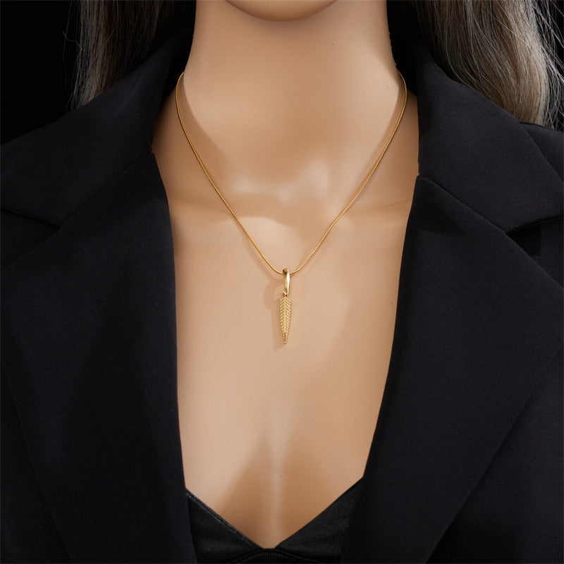 Mannequin wearing a gold necklace with a feather pendant against a black background